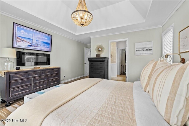 bedroom featuring a raised ceiling, a chandelier, crown molding, wood finished floors, and ensuite bath