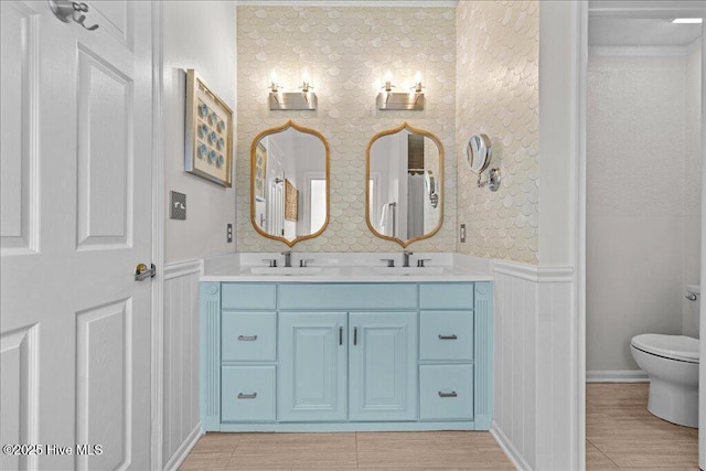 full bath featuring wainscoting, toilet, double vanity, and a decorative wall