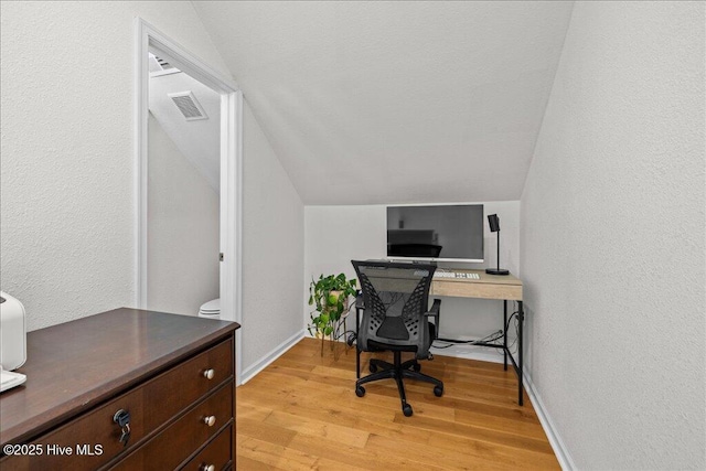 office space with vaulted ceiling, light wood finished floors, a textured wall, and baseboards