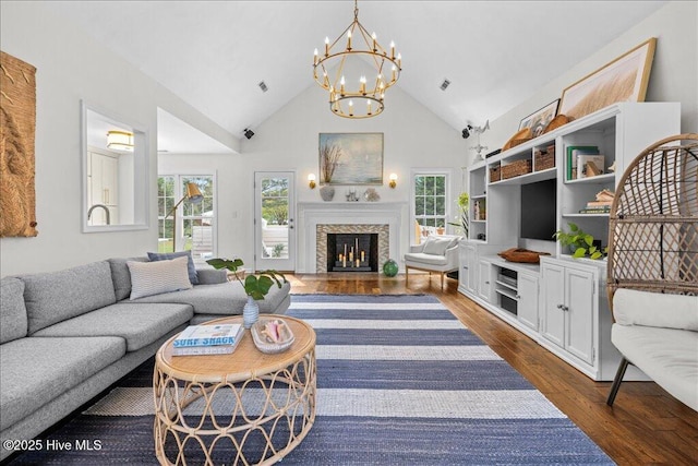 living room with plenty of natural light, high vaulted ceiling, a chandelier, dark wood-style floors, and a fireplace with flush hearth