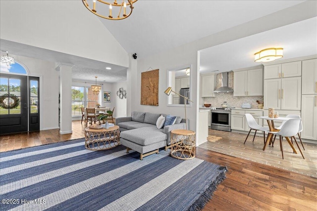 living area featuring a chandelier, hardwood / wood-style flooring, high vaulted ceiling, and ornate columns