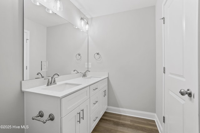 bathroom with double vanity, wood finished floors, baseboards, and a sink