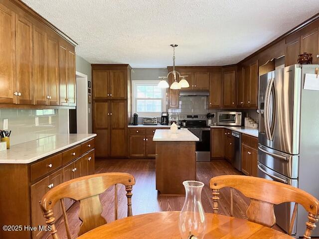 kitchen featuring backsplash, a kitchen island, dark wood-style flooring, appliances with stainless steel finishes, and under cabinet range hood