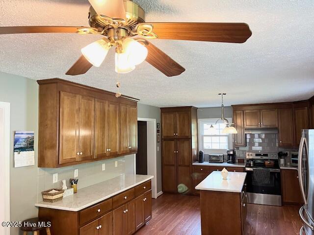kitchen with ceiling fan, a textured ceiling, a center island, stainless steel appliances, and dark wood-style floors
