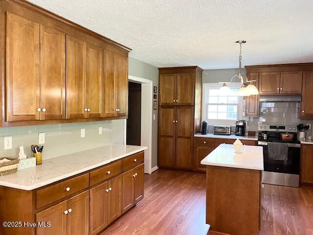 kitchen with stainless steel electric range, dark wood finished floors, brown cabinetry, and tasteful backsplash