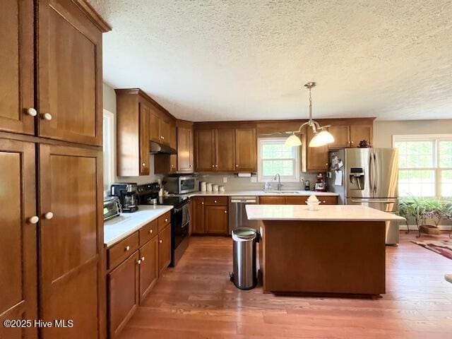 kitchen featuring a sink, a textured ceiling, under cabinet range hood, and stainless steel appliances