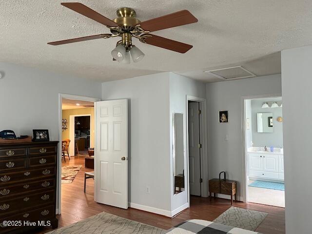 bedroom with wood finished floors, baseboards, ceiling fan, connected bathroom, and a textured ceiling
