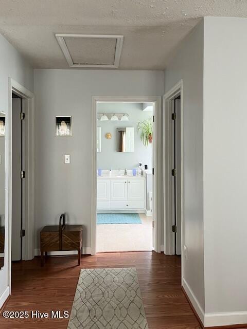 hall featuring baseboards, a sink, wood finished floors, and attic access