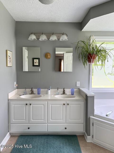 bathroom featuring a sink, a bath, double vanity, and a textured ceiling
