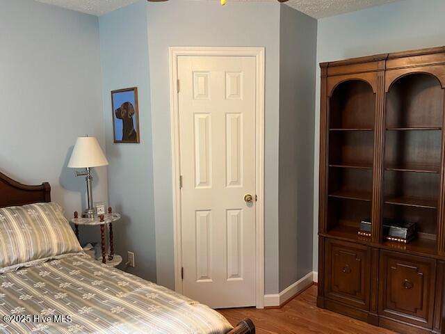 bedroom featuring baseboards, a textured ceiling, and wood finished floors