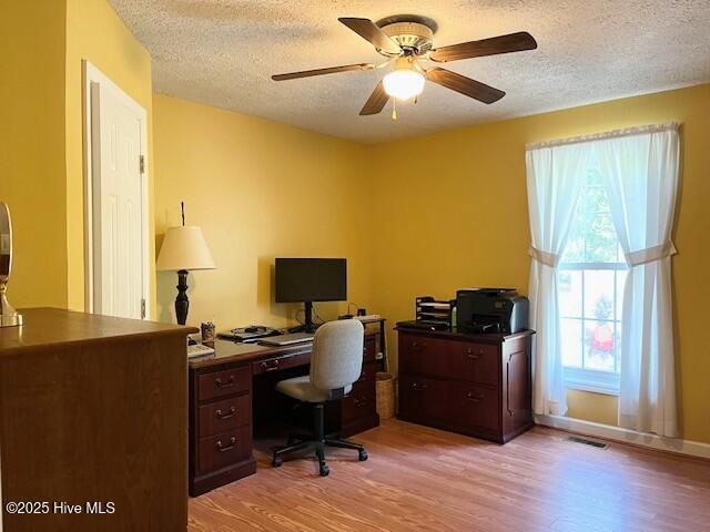 office area with a ceiling fan, a textured ceiling, visible vents, and light wood-type flooring