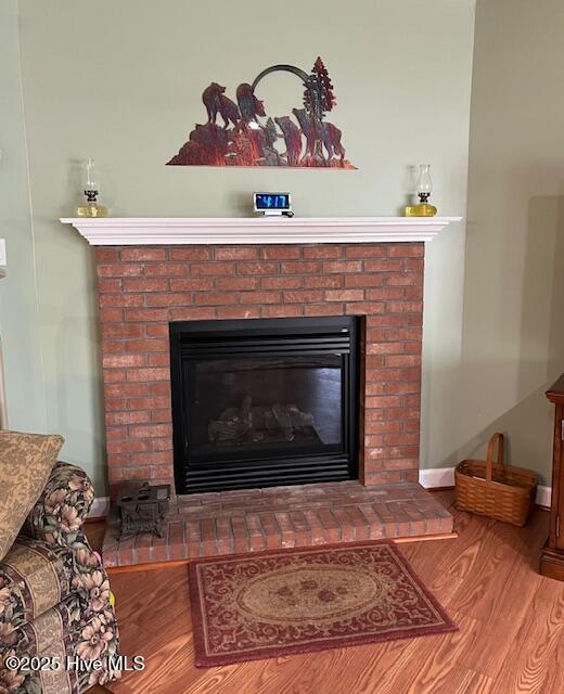 room details featuring baseboards, a brick fireplace, and wood finished floors