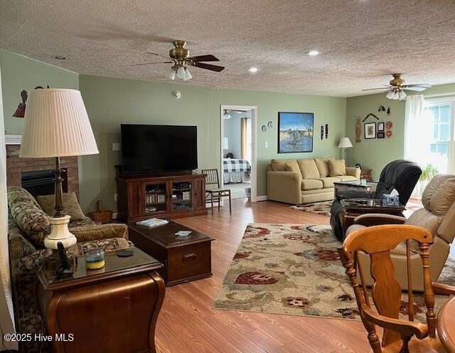 living area with a ceiling fan, a textured ceiling, wood finished floors, and a fireplace