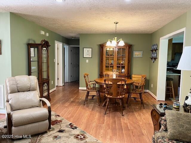 dining area featuring light wood-style floors, a textured ceiling, baseboards, and an inviting chandelier