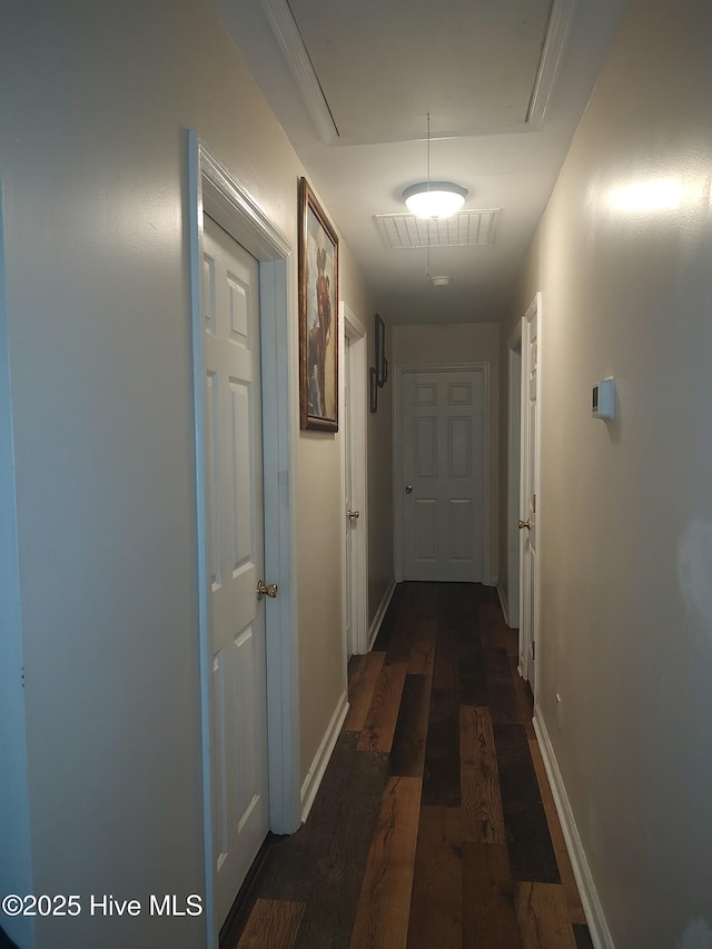 corridor with attic access, dark wood-type flooring, and baseboards