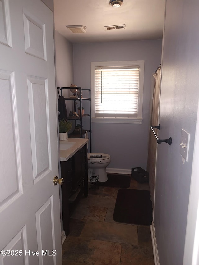 bathroom with toilet, stone finish floors, vanity, and baseboards
