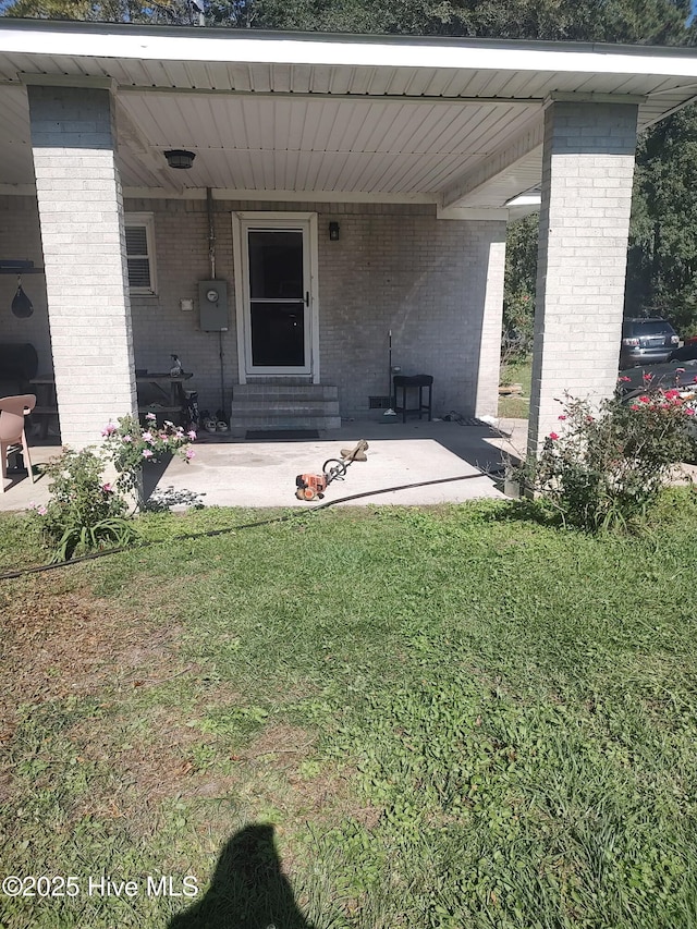 entrance to property featuring a yard and brick siding
