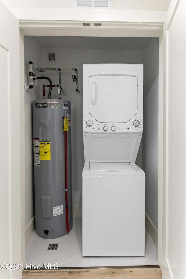 washroom featuring electric water heater, stacked washing machine and dryer, and baseboards