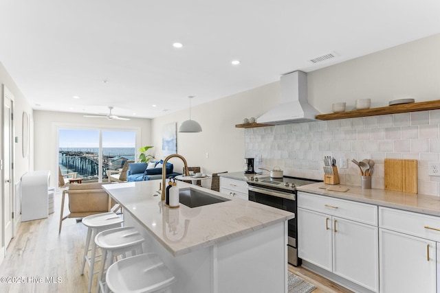 kitchen with stainless steel electric range oven, open shelves, custom exhaust hood, a sink, and light wood-style flooring