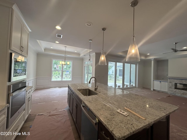 kitchen featuring stainless steel appliances, a sink, a raised ceiling, a wainscoted wall, and open floor plan