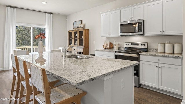 kitchen featuring a sink, appliances with stainless steel finishes, a center island with sink, dark wood finished floors, and white cabinetry