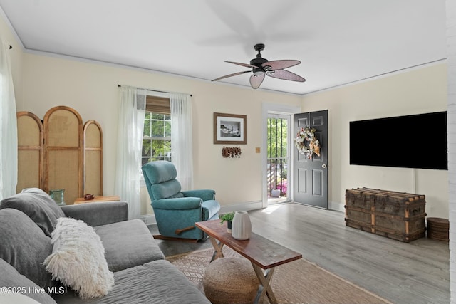 living area with wood finished floors, a ceiling fan, crown molding, and baseboards