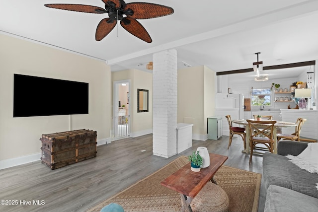 living room with wood finished floors, a ceiling fan, baseboards, and decorative columns