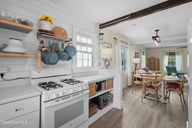 kitchen with white gas range, a wealth of natural light, wood finished floors, and open shelves