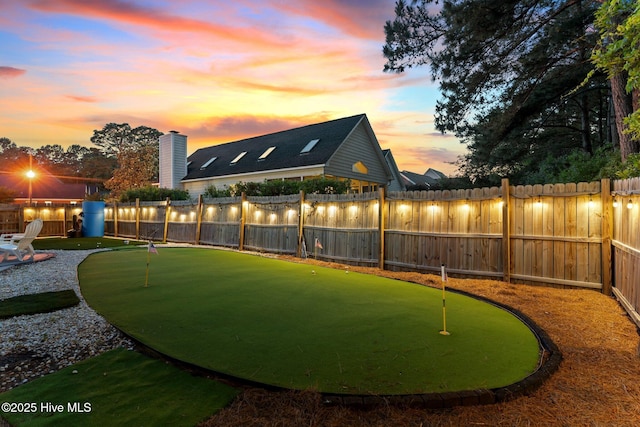 yard at dusk featuring a putting green and a fenced backyard