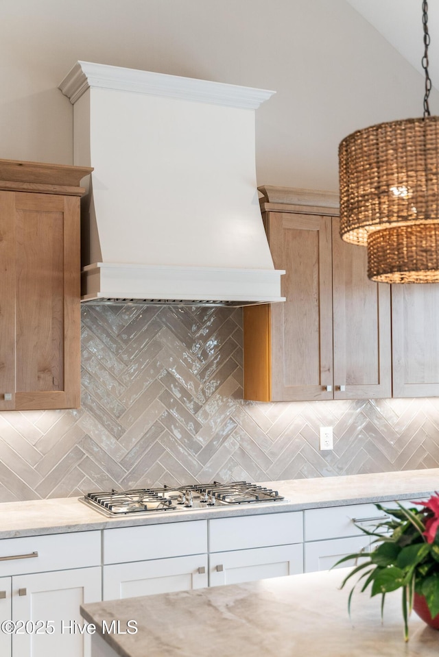 kitchen featuring stainless steel gas cooktop, decorative backsplash, custom exhaust hood, and light stone counters