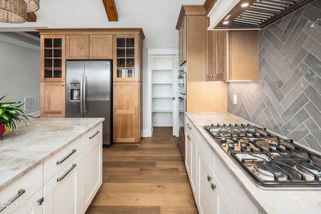 kitchen featuring custom exhaust hood, glass insert cabinets, stainless steel appliances, backsplash, and visible vents