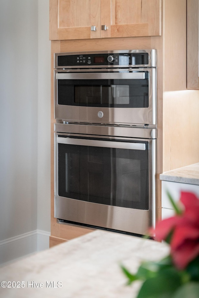interior details with light brown cabinetry, stainless steel double oven, and light countertops