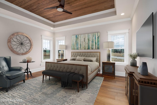 bedroom featuring a tray ceiling, light wood-style flooring, baseboards, and multiple windows