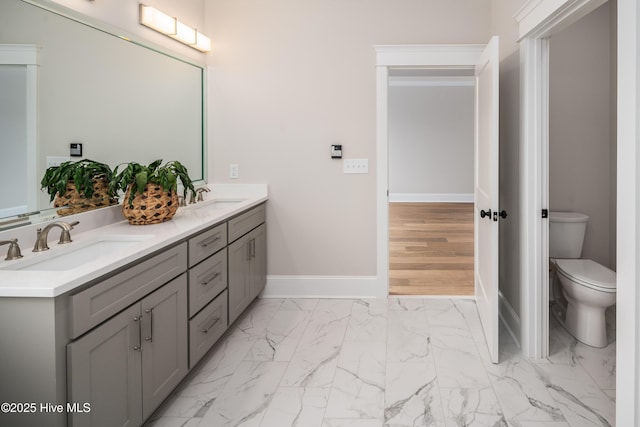 bathroom featuring marble finish floor, double vanity, toilet, a sink, and baseboards