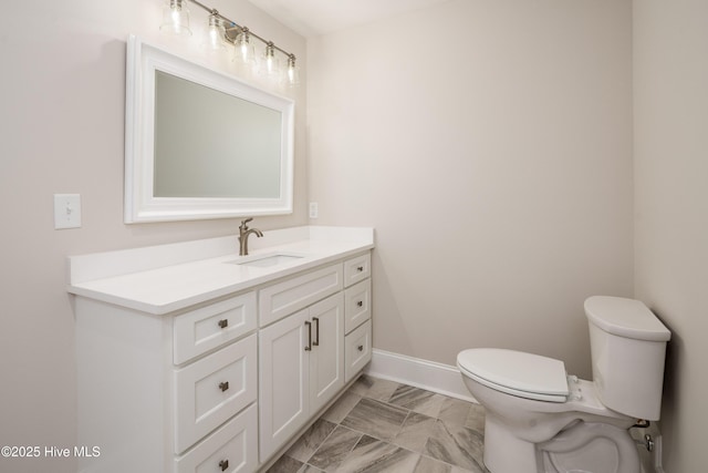 half bath featuring baseboards, marble finish floor, vanity, and toilet