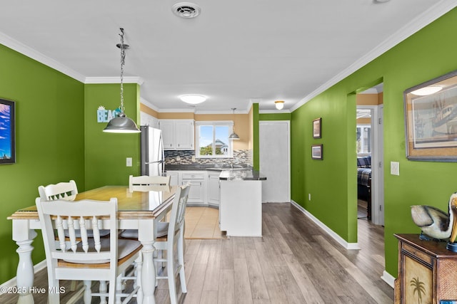 2714 W Beach Dr # 104, Oak Island, NC 28465 - dining room featuring light wood finished floors, baseboards, visible vents, and crown molding