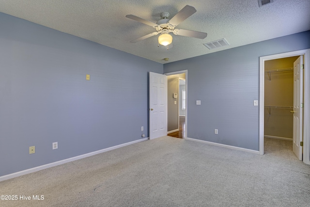 unfurnished bedroom with carpet floors, a textured ceiling, visible vents, and a walk in closet