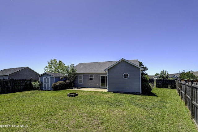 rear view of house with a fenced backyard, a lawn, a fire pit, and a shed