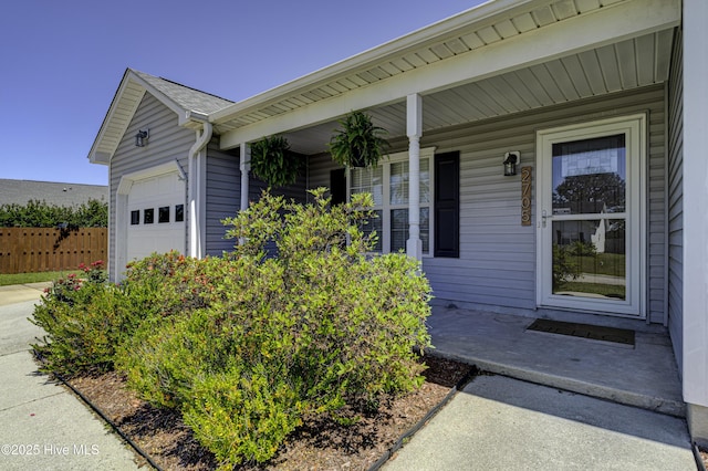 entrance to property featuring a garage, fence, and covered porch