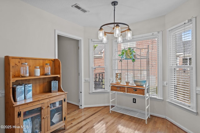 unfurnished dining area with baseboards, hardwood / wood-style flooring, a chandelier, and visible vents
