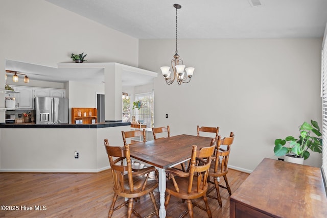 dining space with baseboards, a notable chandelier, lofted ceiling, and light wood-style floors