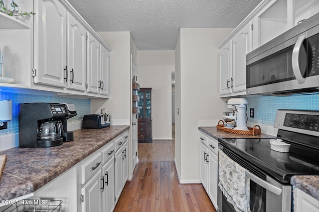 kitchen with dark countertops, appliances with stainless steel finishes, tasteful backsplash, wood finished floors, and white cabinetry
