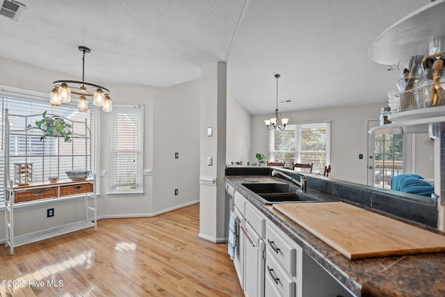 kitchen featuring a notable chandelier, a sink, a textured ceiling, light wood-type flooring, and visible vents