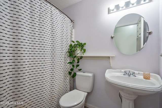 full bathroom featuring curtained shower, toilet, baseboards, a textured ceiling, and a sink