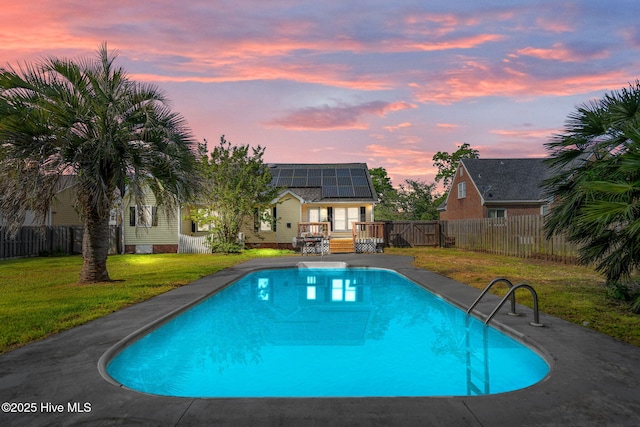 pool at dusk with a lawn, a fenced in pool, a fenced backyard, and a deck