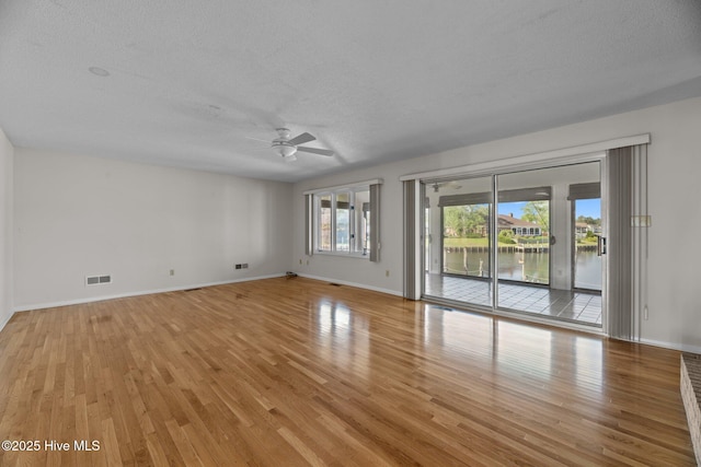 spare room featuring visible vents, baseboards, light wood-type flooring, a textured ceiling, and a ceiling fan
