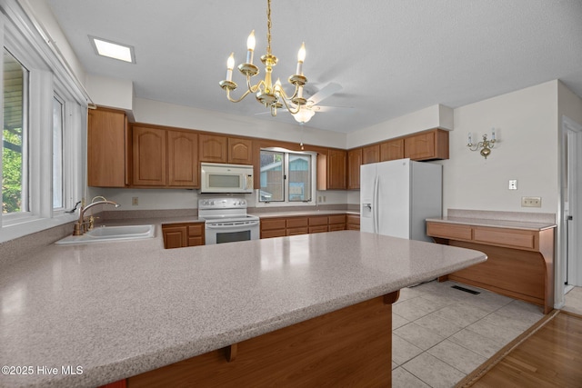 kitchen with a sink, a peninsula, white appliances, and light countertops