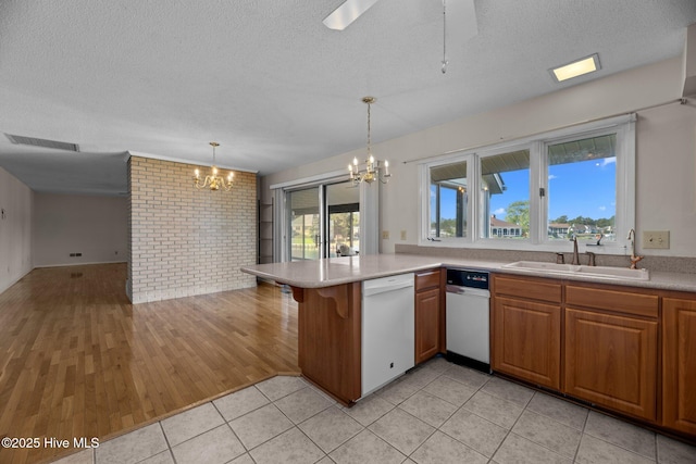 kitchen with brick wall, visible vents, white dishwasher, a sink, and a peninsula