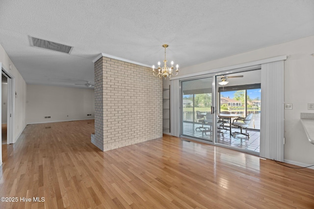 unfurnished dining area featuring a textured ceiling, visible vents, wood finished floors, and ceiling fan with notable chandelier