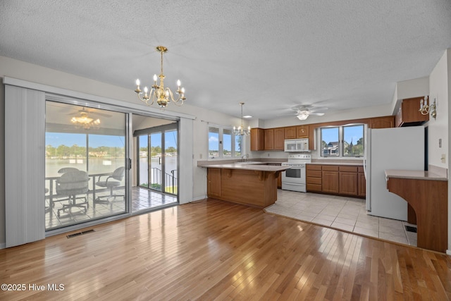 kitchen featuring visible vents, brown cabinets, a peninsula, white appliances, and light wood-style flooring